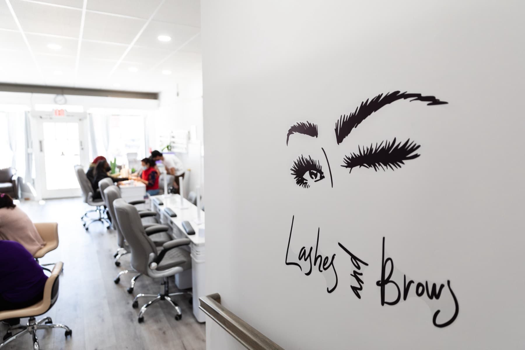 Technicians with clients at the manicure tables, past the lashes and brows room